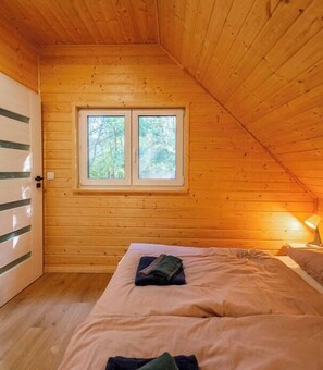 A wooden cabin room with a bed, a window, and a door. - Leno Tu – Scandinavian Cottage with Sauna and Hot Tub (Tuchomie)