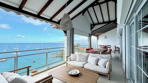 Un balcone con un divano bianco, un tavolo di legno e una zona pranzo con vista sul mare.