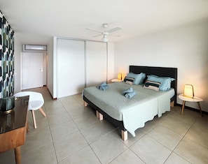 Une chambre à coucher comprenant un lit, des tables de chevet, un ventilateur de plafond et un bureau avec une chaise.