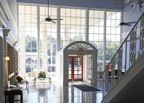 Eine großzügige Lobby mit hohen Decken, großen Fenstern und einer zentral gelegenen roten Tür, die zu einem Ausgang führt.