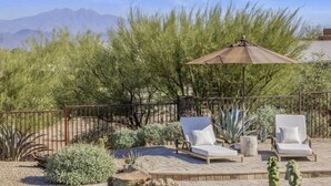 A patio with two lounge chairs, a wooden table, and an umbrella. - Ranch Road Desert Oasis...Privacy...Unbelievable Mountain Views! (Scottsdale)
