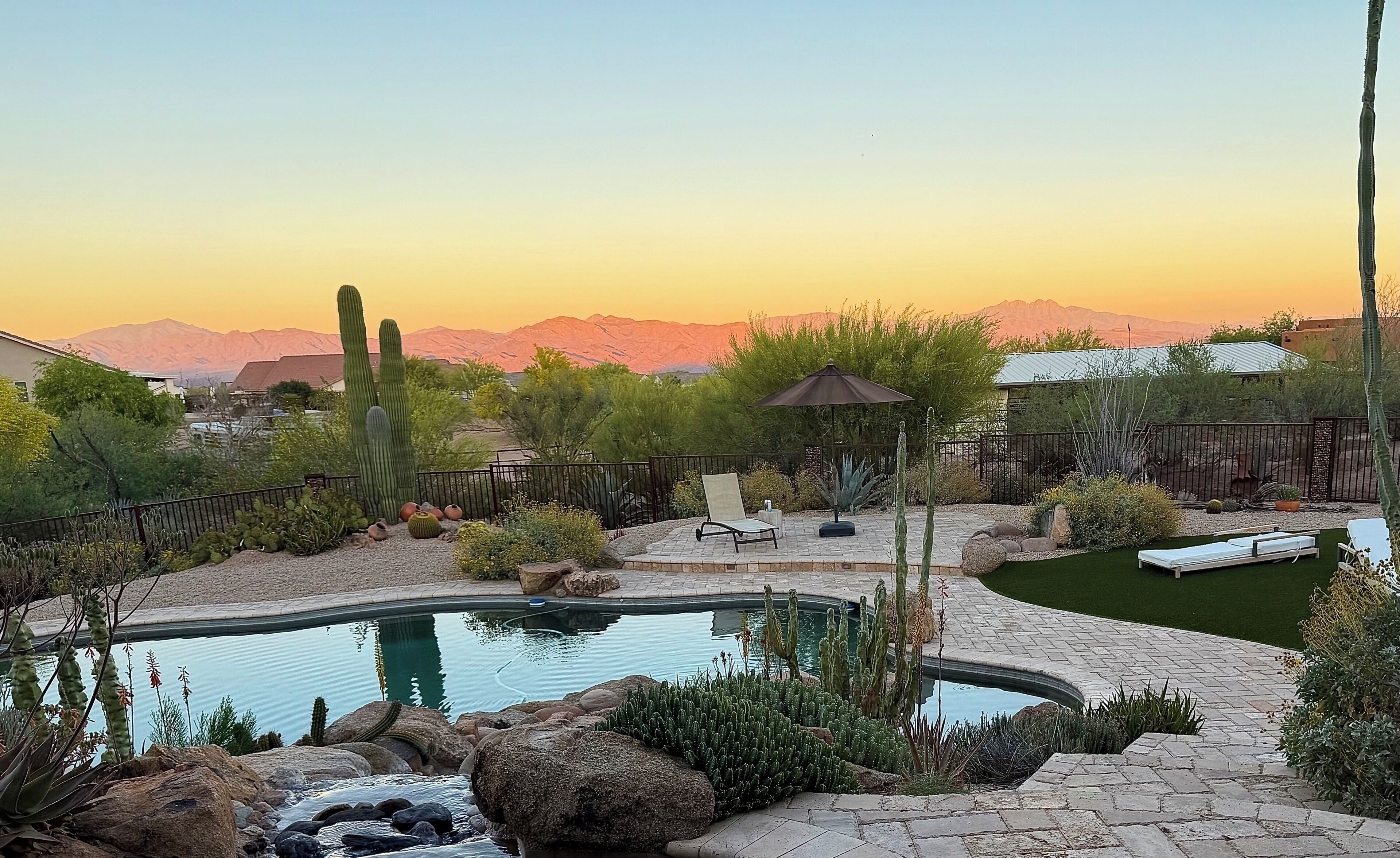 A backyard with a swimming pool, surrounded by desert plants and a view of mountains.