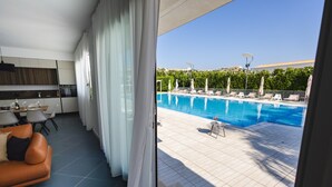 Ein modernes Wohnzimmer mit einer Couch, einem Esstisch und Blick auf ein Schwimmbad mit Liegestühlen.