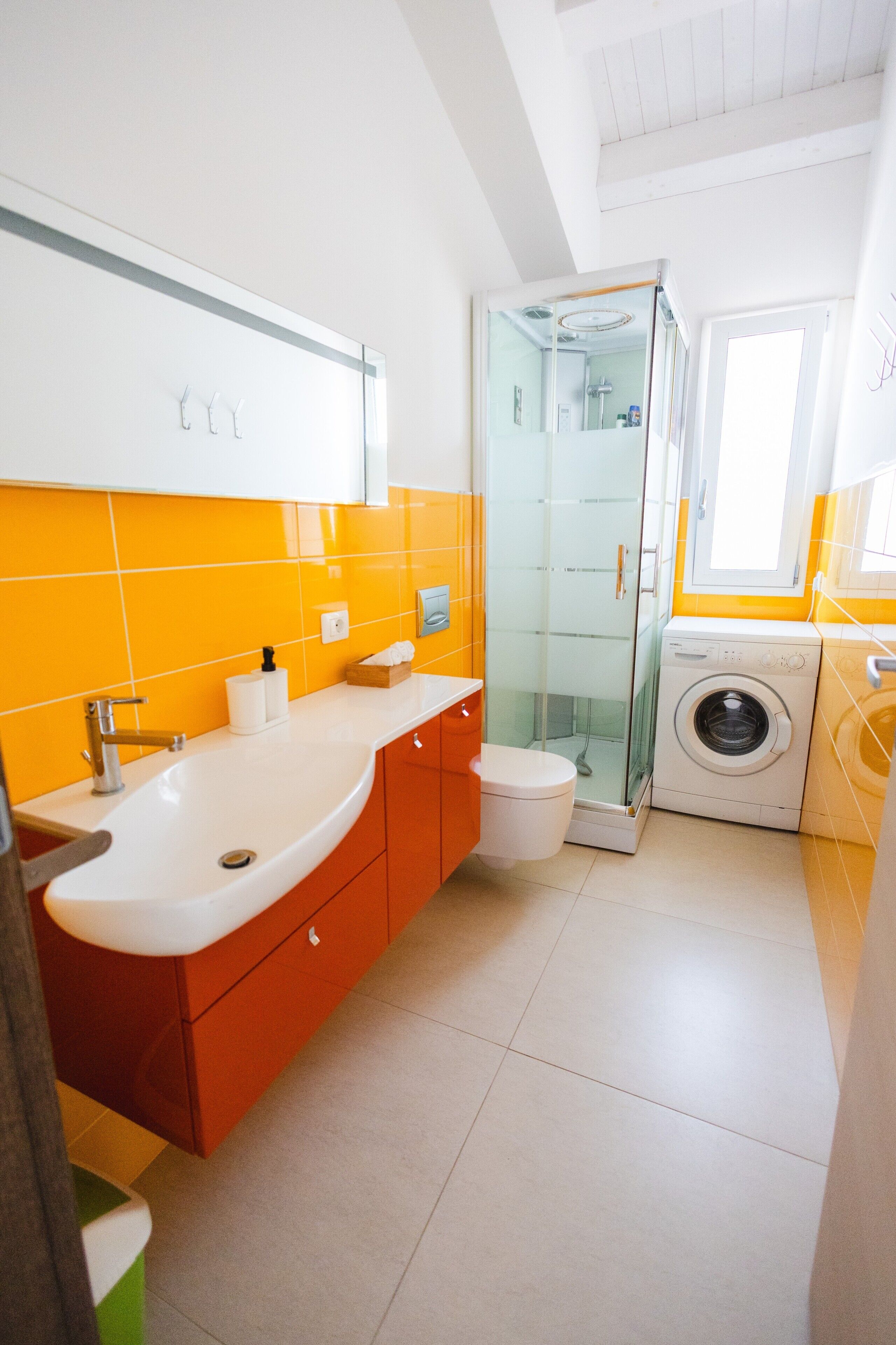 Ein kleines Badezimmer mit Waschbecken, Toilette, Duschkabine aus Glas und einer Waschmaschine.