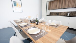 Ein modernes Esszimmer mit einem Holztisch, gedecktem Essen, weißen Stühlen und einer Küchenzeile mit Holzrückwand.