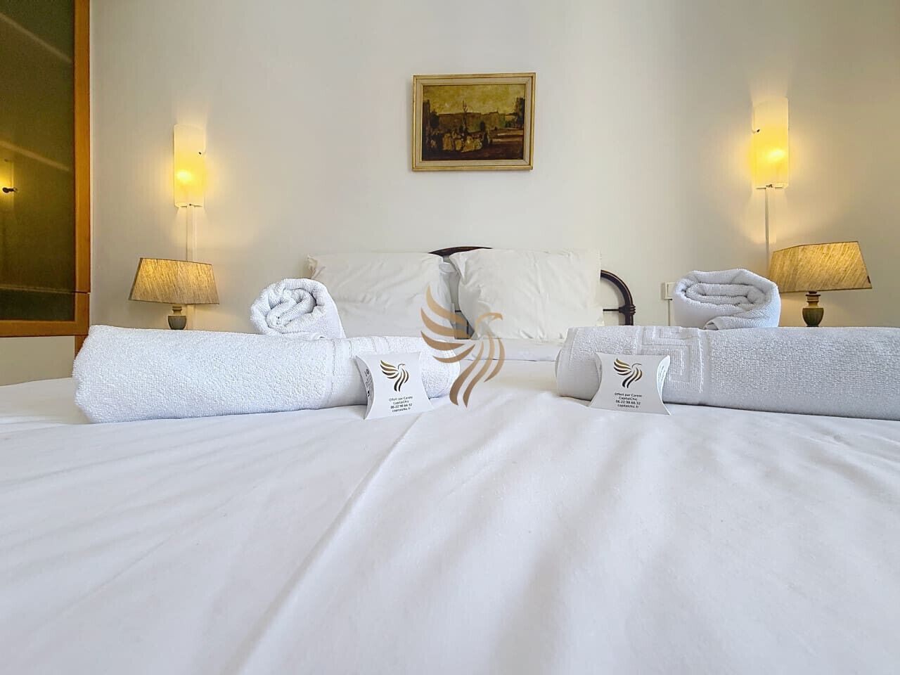 Een hotelkamer met een net opgemaakt bed, twee wandlampen, een schilderij aan de muur en een grote spiegel aan de linkerkant.