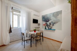 Ein modernes Zimmer mit Esstisch, Stühlen, Fernseher und einem großen abstrakten Gemälde an der Wand.