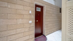 En hall med beige tegelväggar, en trädörr med en skylt och ett vitt kakelgolv.