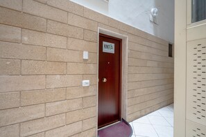 A hallway with beige brick walls, a wooden door with a sign, and a white tiled floor. - Apartment 'Kaktus 2 - Music' with Wi-Fi and Air Conditioning (Bari)