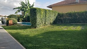 A well-maintained garden with a swimming pool, a paved walkway, and a building with a tiled roof. - Casa Jasmim - Tranquil Refuge (Algueirão-Mem Martins)