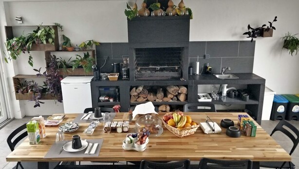 A kitchen with a built-in oven, wooden table, chairs, and various kitchen items. - Casa Jasmim - Tranquil Refuge (Algueirão-Mem Martins)