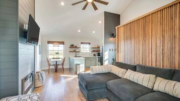 A spacious living area with a large sectional sofa, a dining table with chairs, a kitchen in the background, and a ceiling fan.