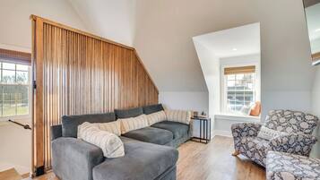 A loft-style room with a grey sectional sofa, a patterned armchair, and a wooden slatted partition.
