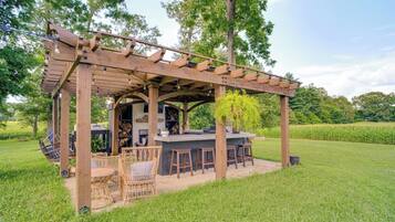 An outdoor bar area with a pergola, seating, and a grill.
