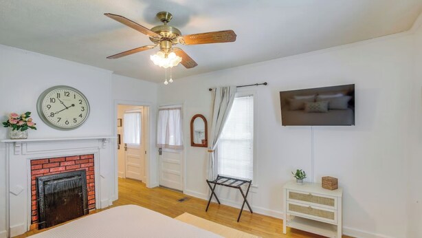 A bedroom with a bed, a ceiling fan, a clock, a fireplace, a TV, and a window with curtains. - Little Farm House with Shaded Front Porch, Fire Pit, Covered Parking (Cross Plains)