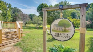 A wooden sign with 'THE LITTLE FARMHOUSE' written on it, surrounded by a wooden structure and a grassy area. - Little Farm House with Shaded Front Porch, Fire Pit, Covered Parking (Cross Plains)