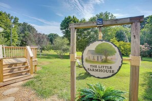 Un senyal de fusta amb la frase 'THE LITTLE FARMHOUSE', envoltat d'una estructura de fusta i una zona verda.