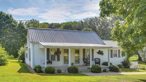 A single-story house with a porch, a small garden, and a metal roof. - Little Farm House with Shaded Front Porch, Fire Pit, Covered Parking (Cross Plains)