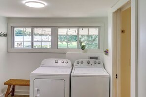 Una sala de bugaderia amb dues rentadores i assecadores frontals de color blanc, una banca de fusta, una finestra amb vista a un pati i una porta a la dreta.