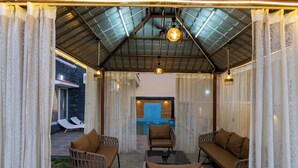 Um pátio externo com móveis de vime, piscina e área coberta com telhado metálico.