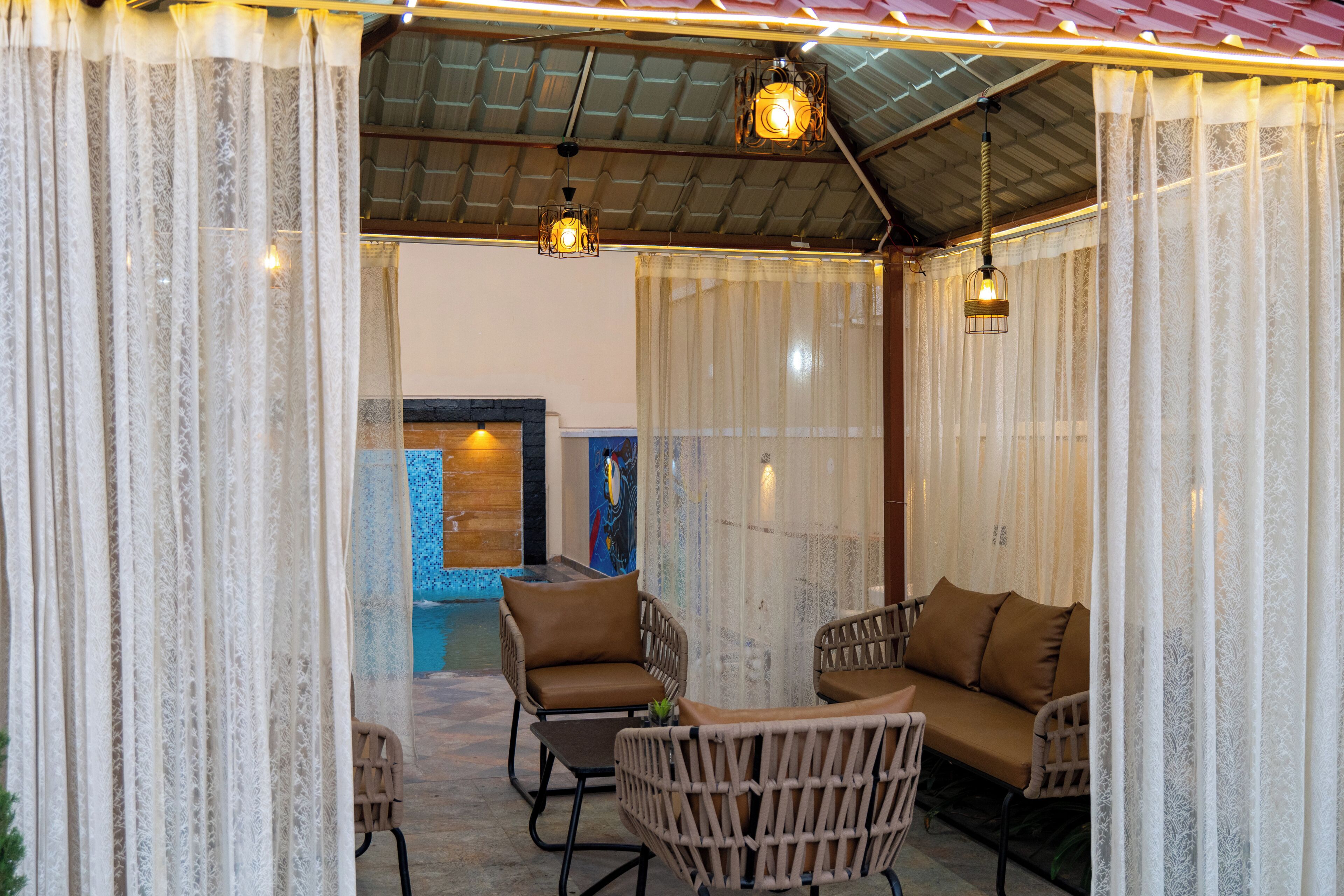 A covered outdoor seating area with wicker furniture and a pool in the background.