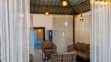 A covered outdoor seating area with wicker furniture and a pool in the background.