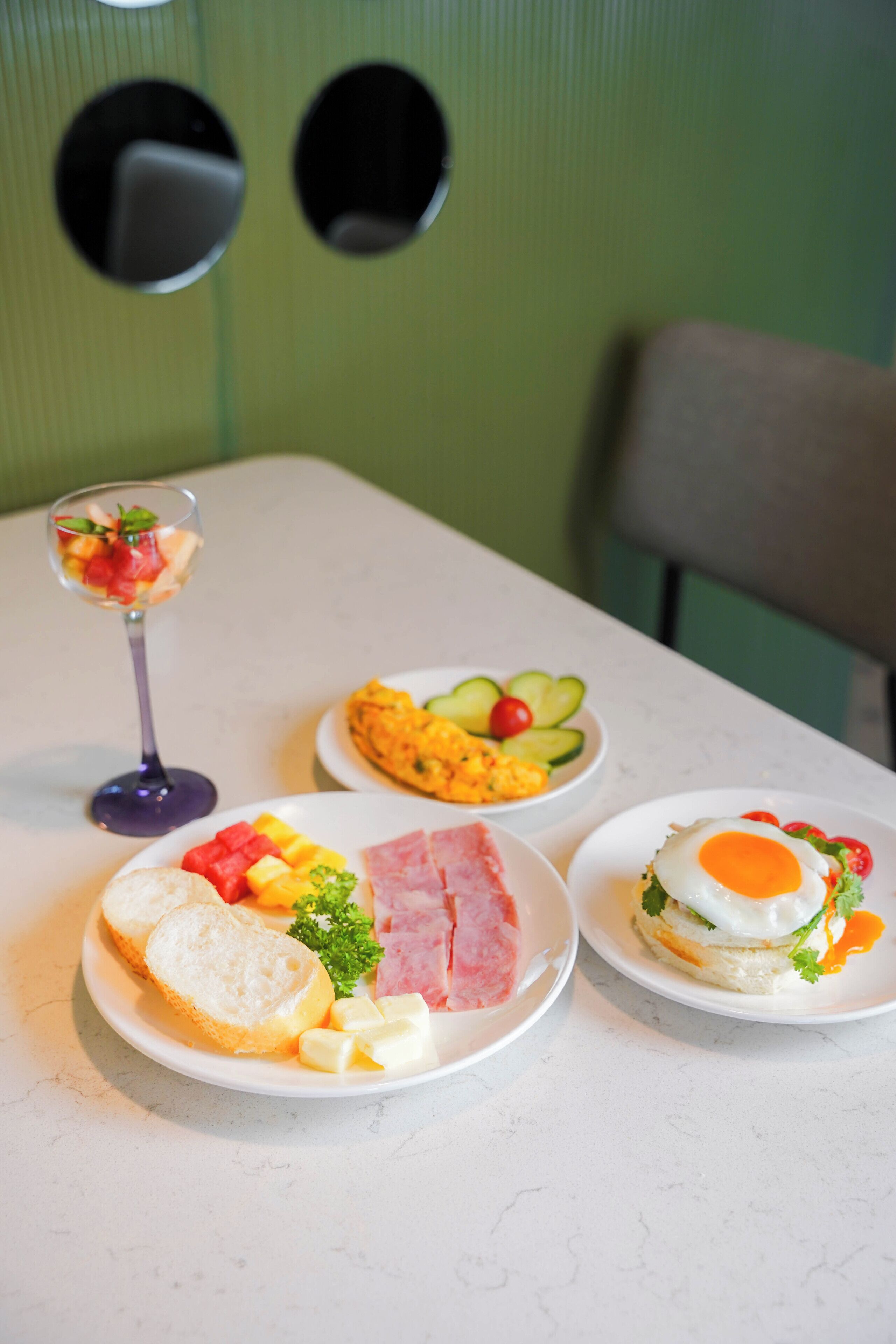 Een tafel met drie borden eten, een glas drinken en een groene muur met twee ronde uitsparingen.