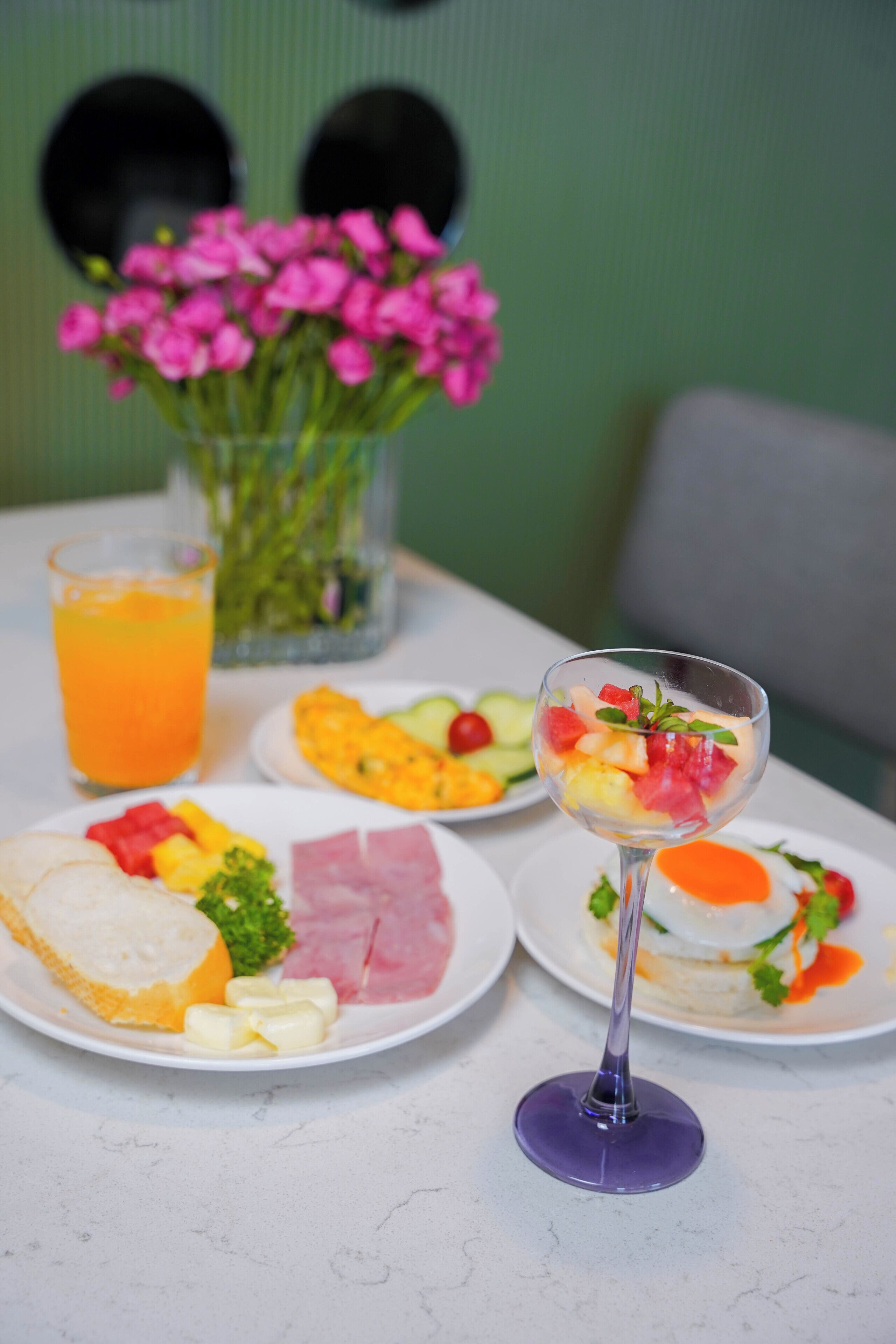 Una mesa con platos de comida, un vaso de jugo de naranja y un florero con flores.