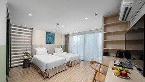 Une chambre d’hôtel avec deux lits, un bureau avec des articles pour le petit-déjeuner, une machine à café et une grande fenêtre avec des rideaux.