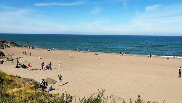 A wide sandy beach with people scattered across it, a clear blue sky, and the ocean in the background.