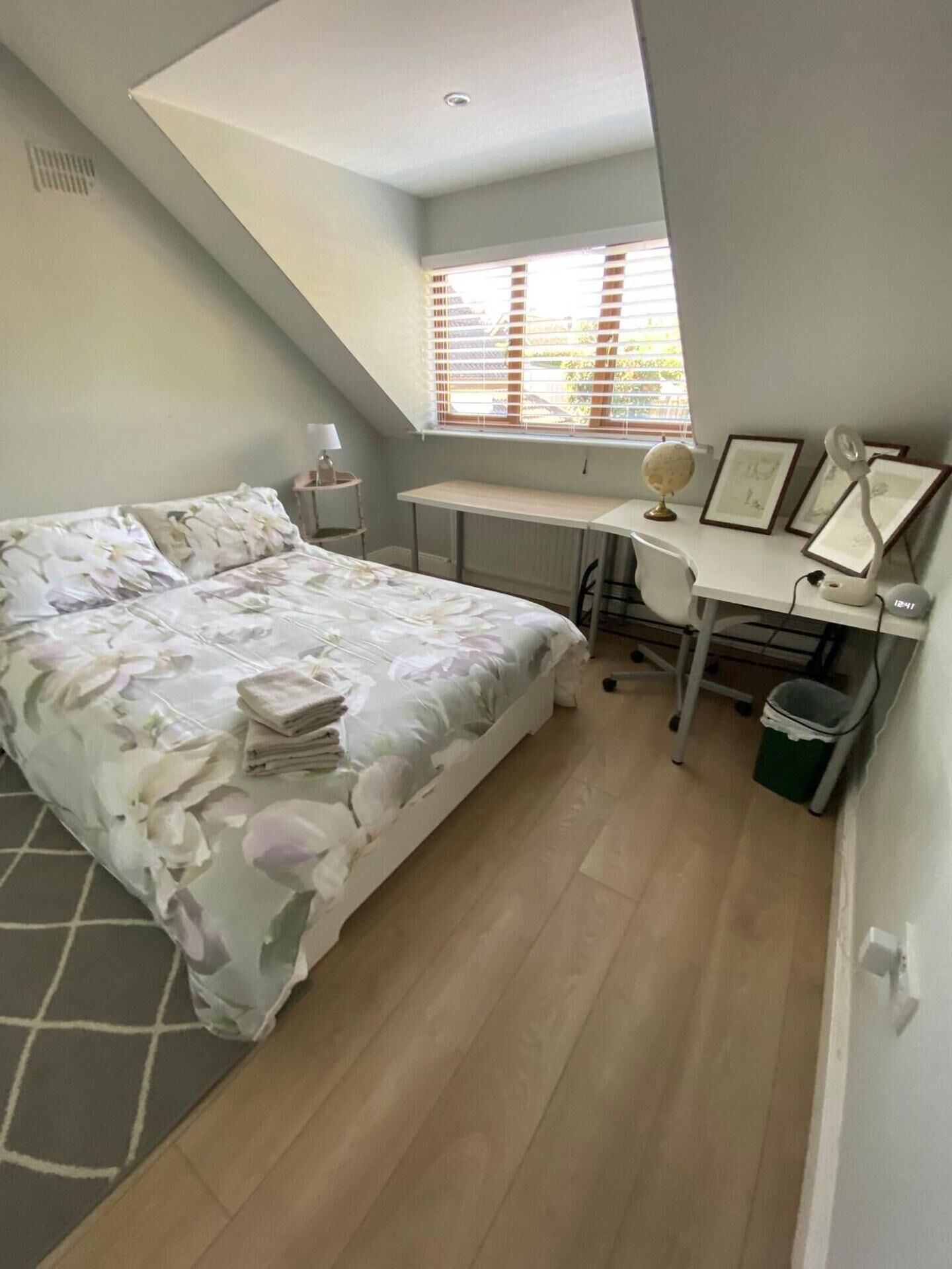 A bedroom with a bed, desk, chair, lamp, globe, and a window with blinds.