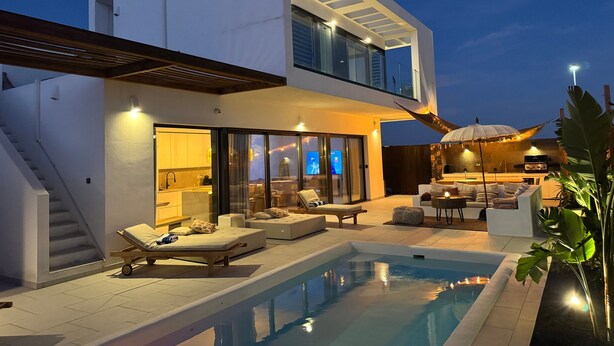 Una casa moderna de dos pisos con piscina, mobiliario exterior y una escalera.