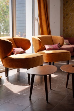 Ein modernes Wohnzimmer mit zwei Sofas, zwei kleinen Tischen, einem großen Fenster mit Vorhängen und einer Wand mit Muster.