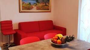 A dining area with a table, red chairs, a red sofa, a painting on the wall, and a fruit bowl on the table. - Large apartment with lake view terrace 5 minutes walk from the center (Bardolino)