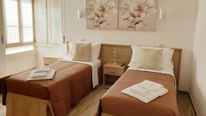 A hotel room with two beds, a wooden floor, a window with blinds, and wall-mounted artwork. - Large apartment with lake view terrace 5 minutes walk from the center (Bardolino)