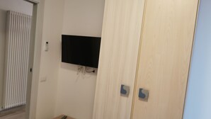 A room with a wooden wardrobe, a television mounted on the wall, and a small wooden table. - Large apartment with lake view terrace 5 minutes walk from the center (Bardolino)