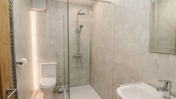 A modern bathroom with a glass-enclosed shower, a toilet, and a sink.