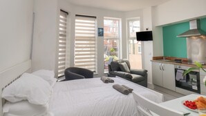 Ein Hotelzimmer mit Bett, Stuhl, einer kleinen Küchenzeile und einem Fernseher.