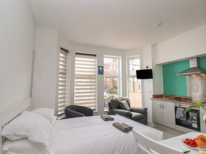 Una habitación de hotel con una cama, una silla, una kitchenette pequeña y un televisor.