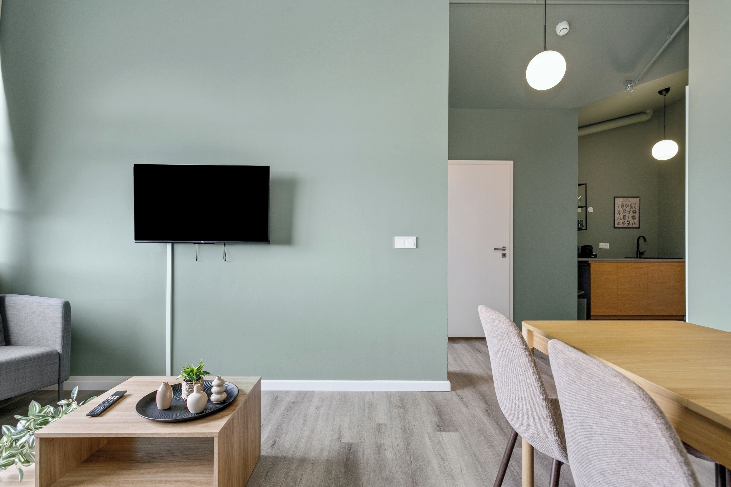 A modern living room with a flat-screen TV, a dining table with chairs, a sofa, and a small coffee table with decorative items.