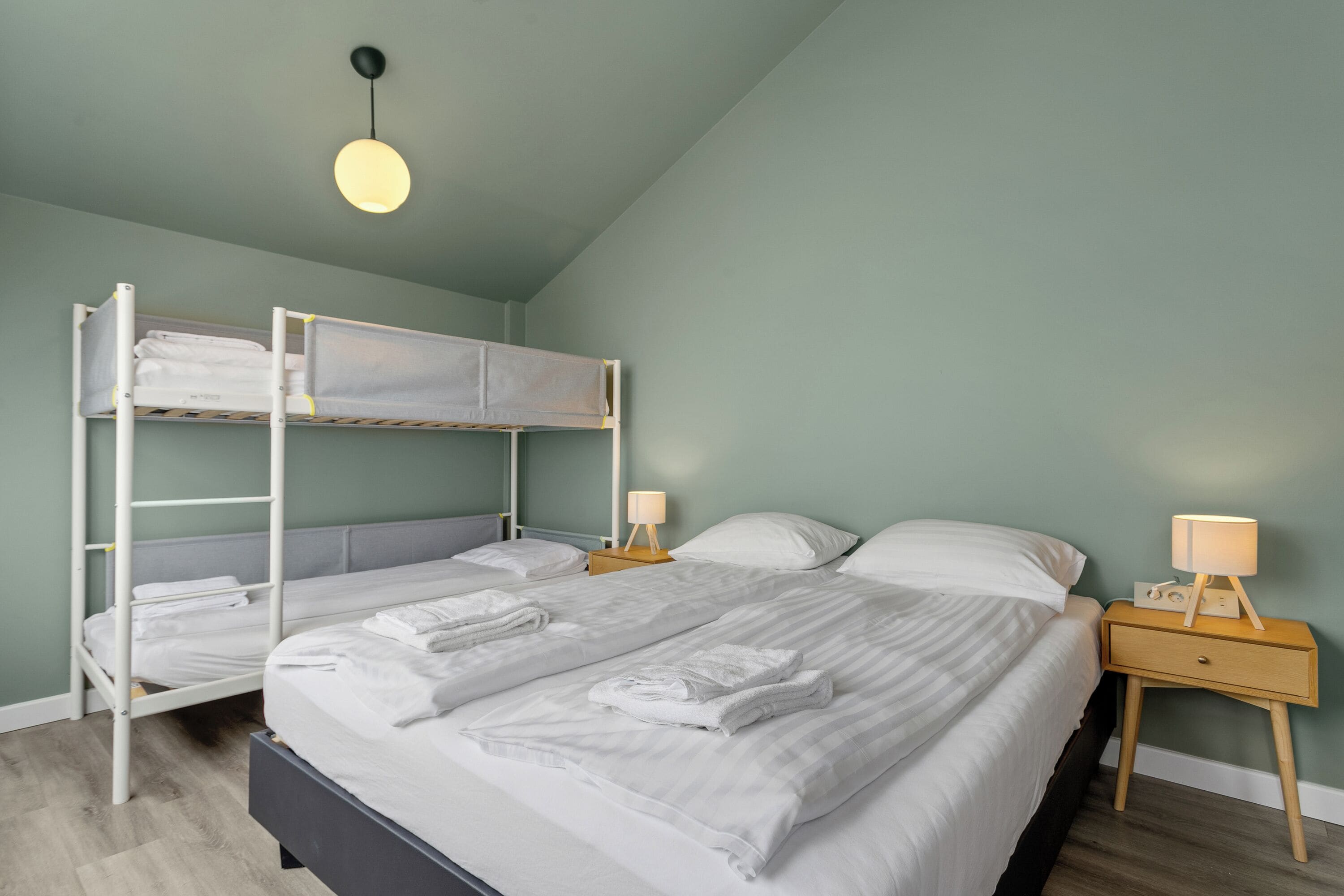 Habitación con literas, una cama individual, una mesita de noche con lámpara y una lámpara colgante.