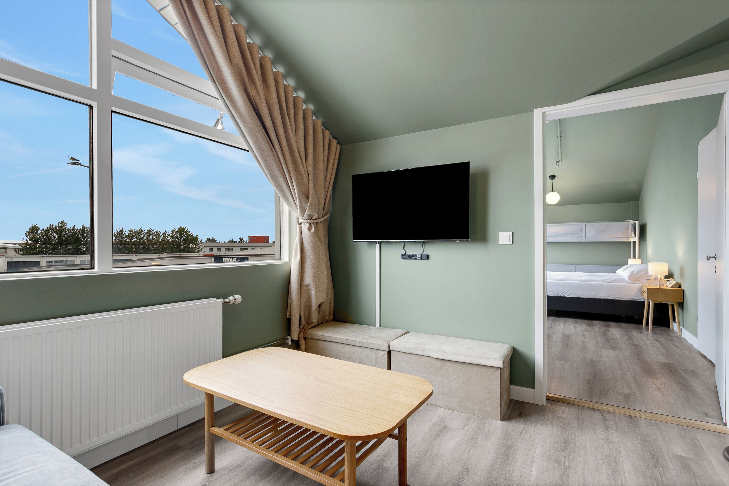 A room with a bed, a TV, a table, and a window with curtains.