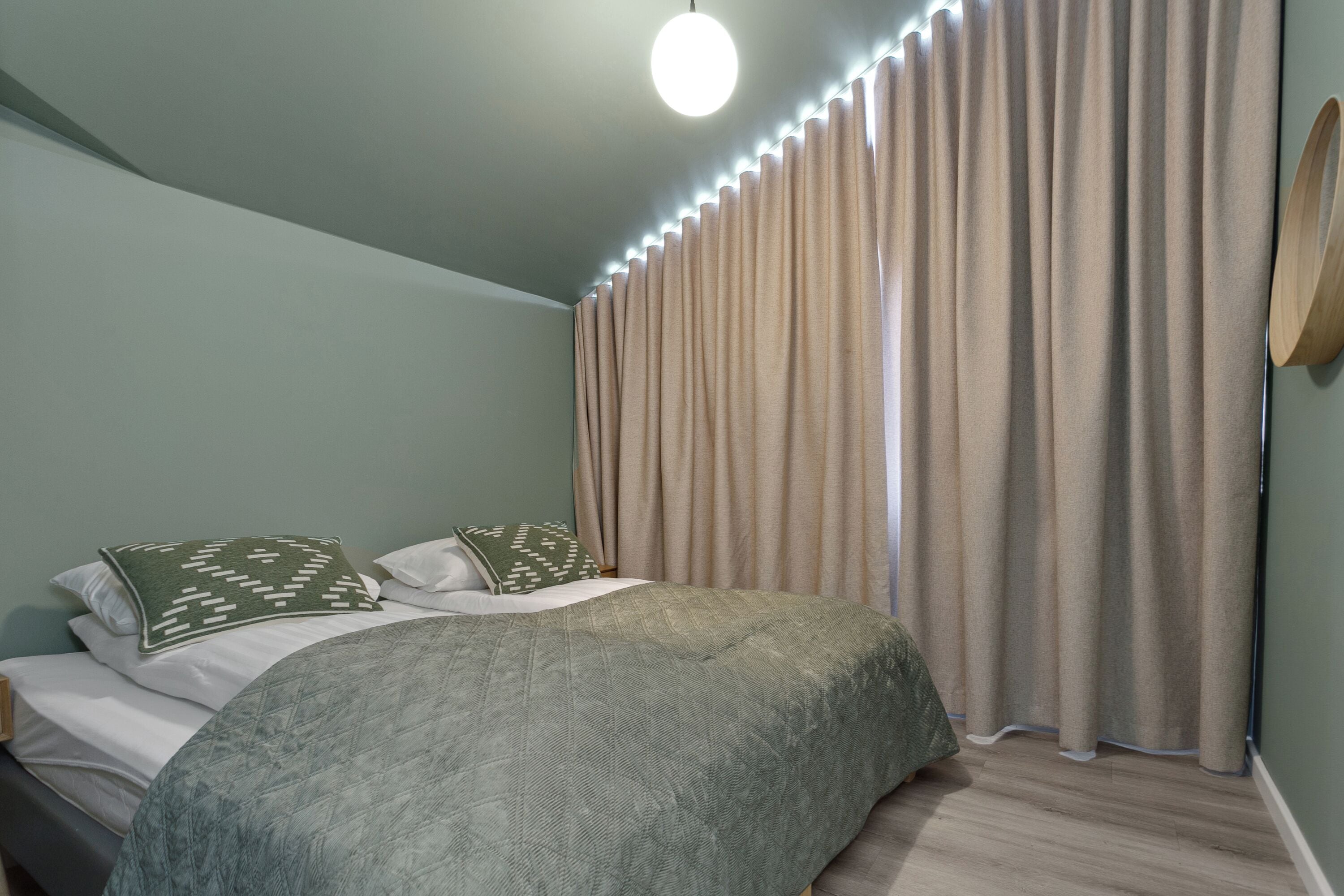 Une chambre à coucher avec un lit, des rideaux, un miroir fixé au mur et un luminaire au plafond.