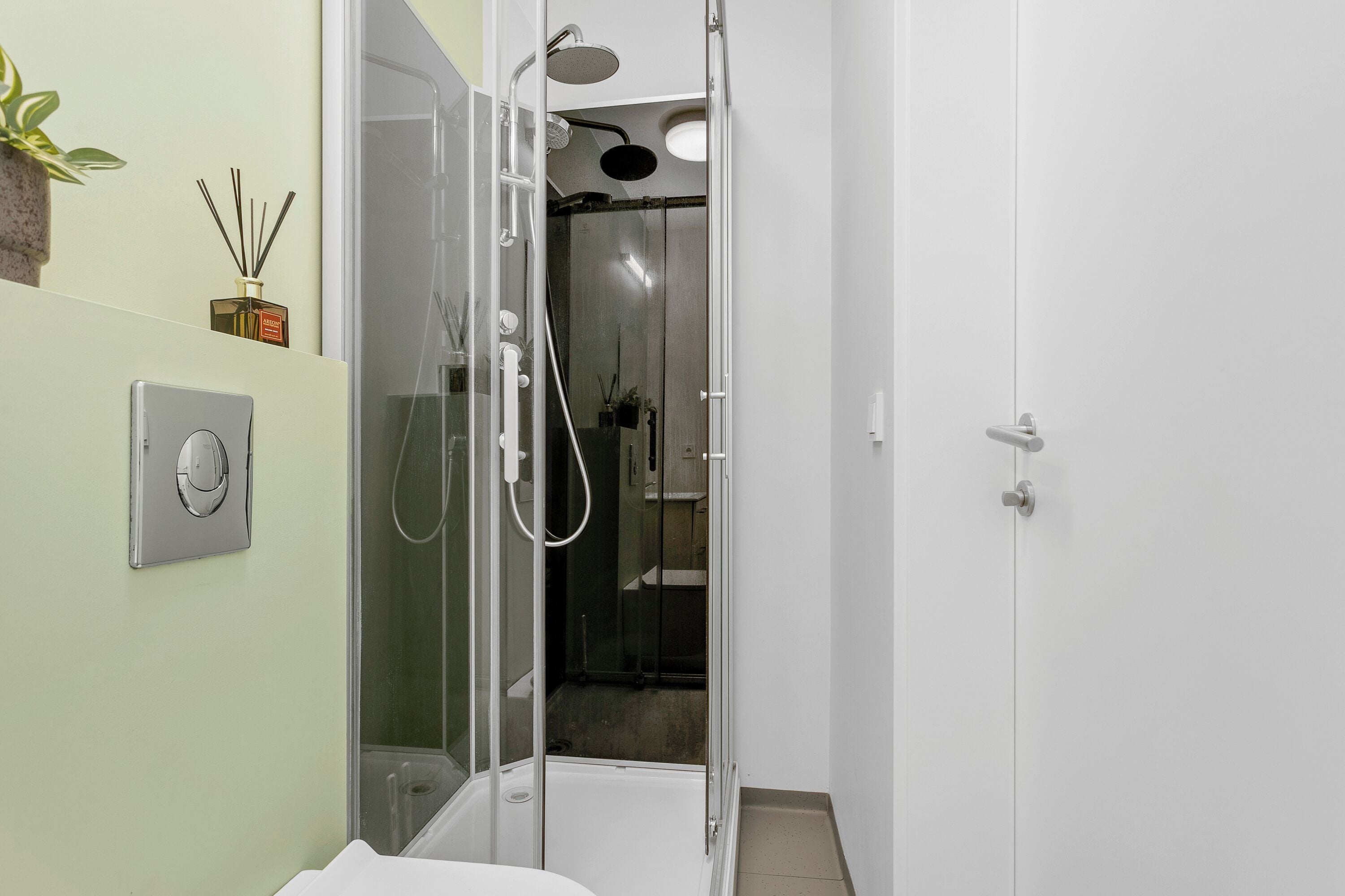 A modern bathroom with a glass-enclosed shower, a white sink, and a potted plant on the wall.