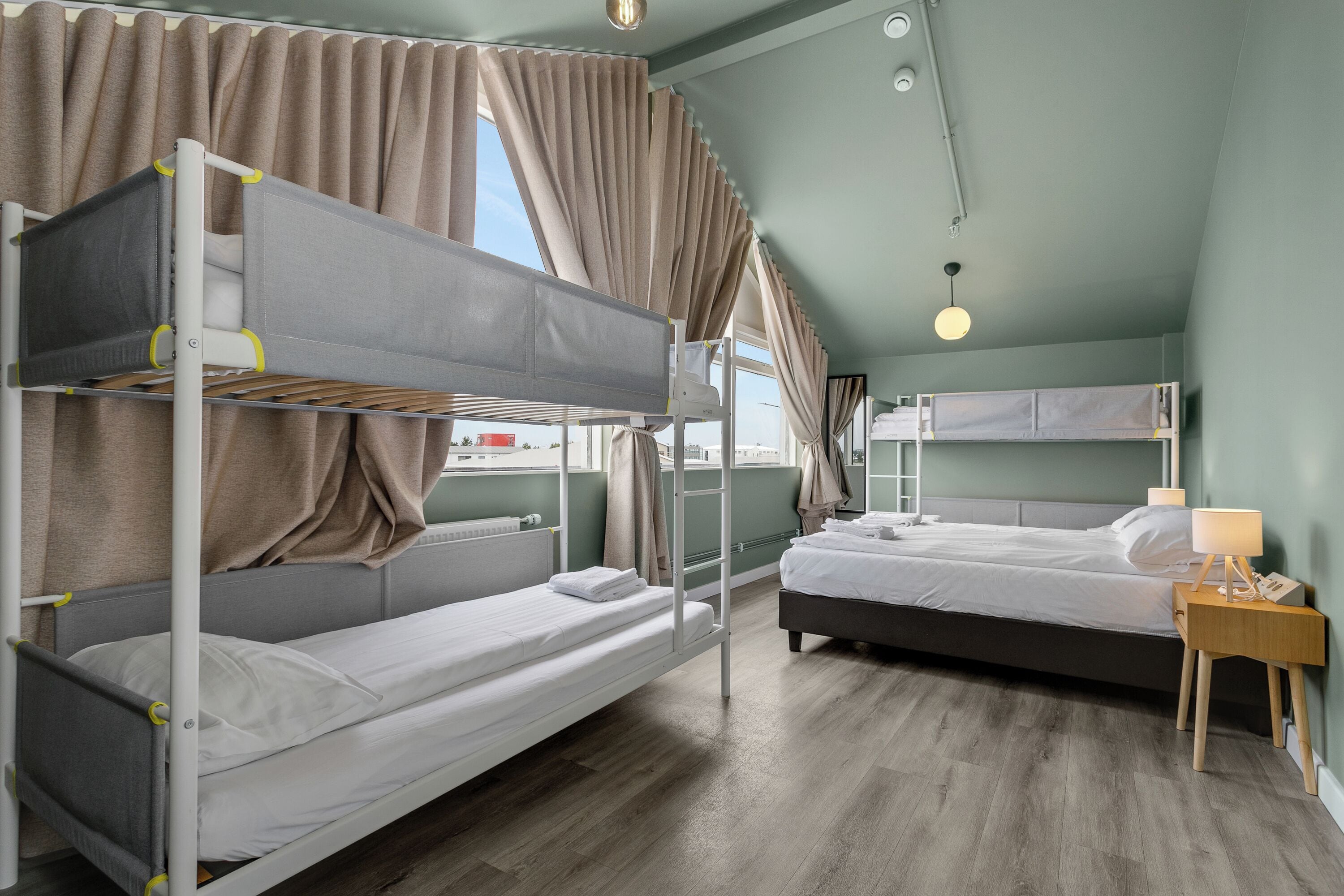 A bunk bed room with a window, a bedside table with a lamp, and a view of the outside.