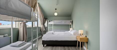 Um quarto com beliches, uma mesa de cabeceira com abajur e uma janela com cortinas.