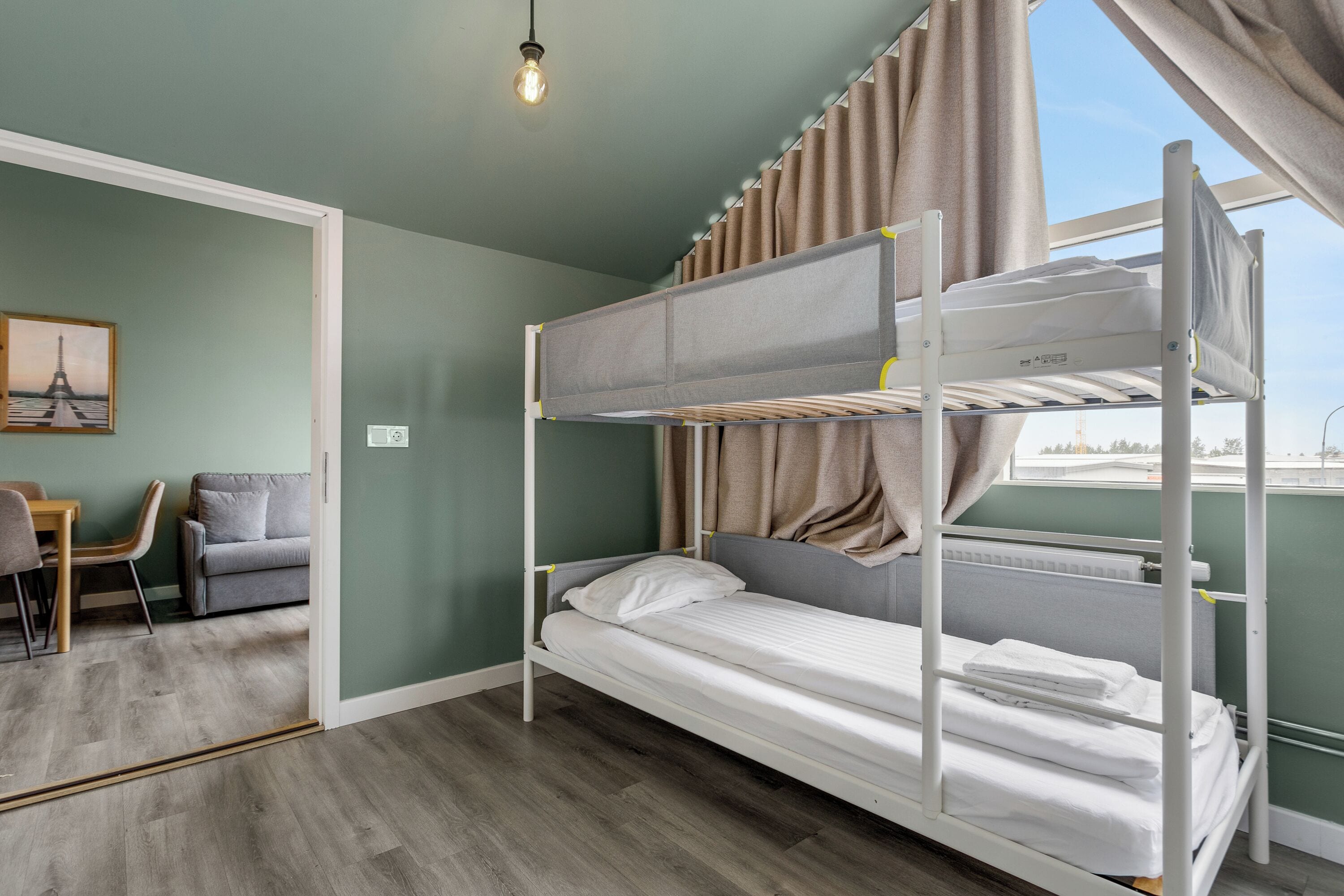 Habitación con literas, un escritorio, una silla, un cuadro en la pared y una ventana con cortinas.