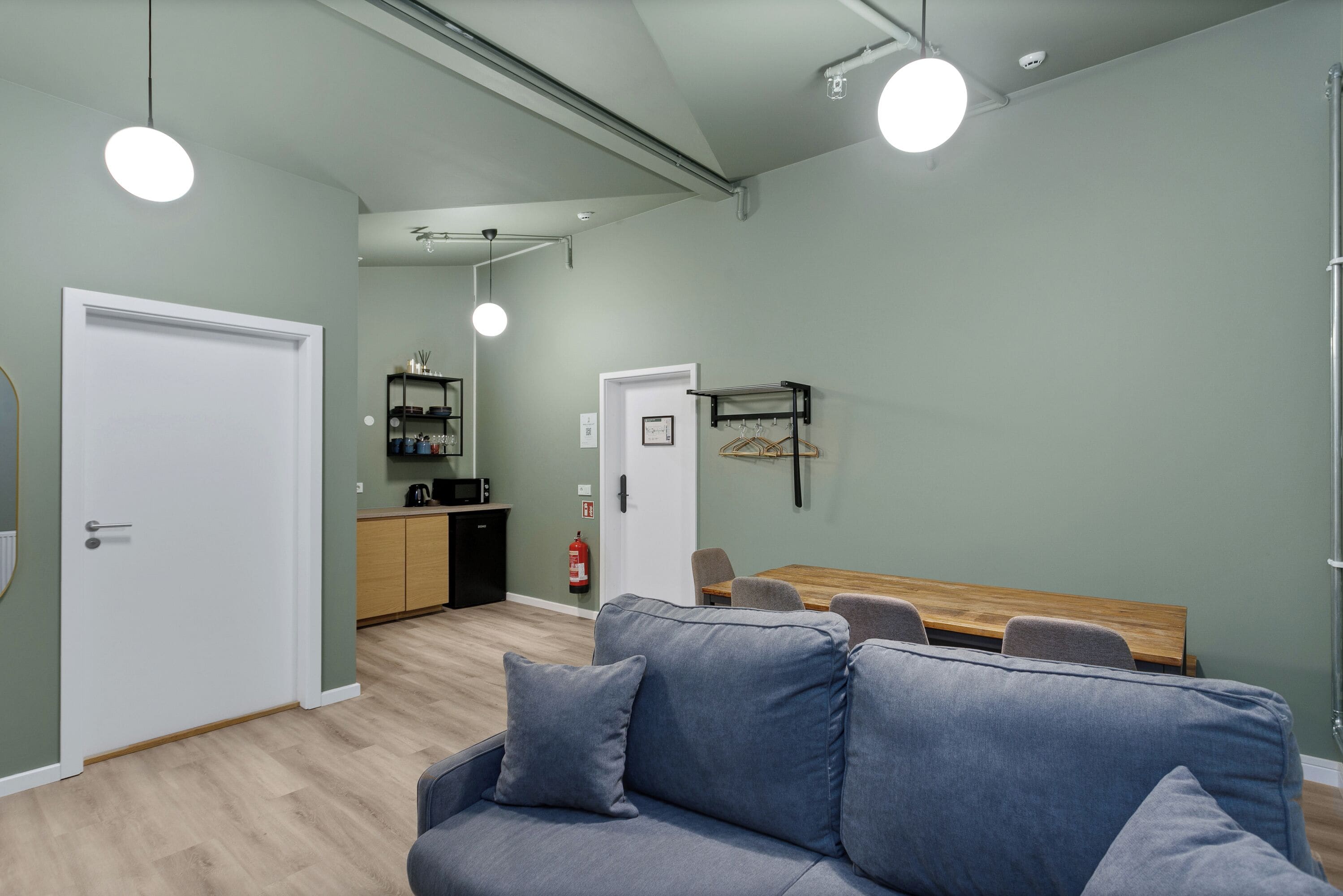 Un salon moderne avec un canapé gris, une table à manger en bois et un coin cuisine à l’arrière-plan.
