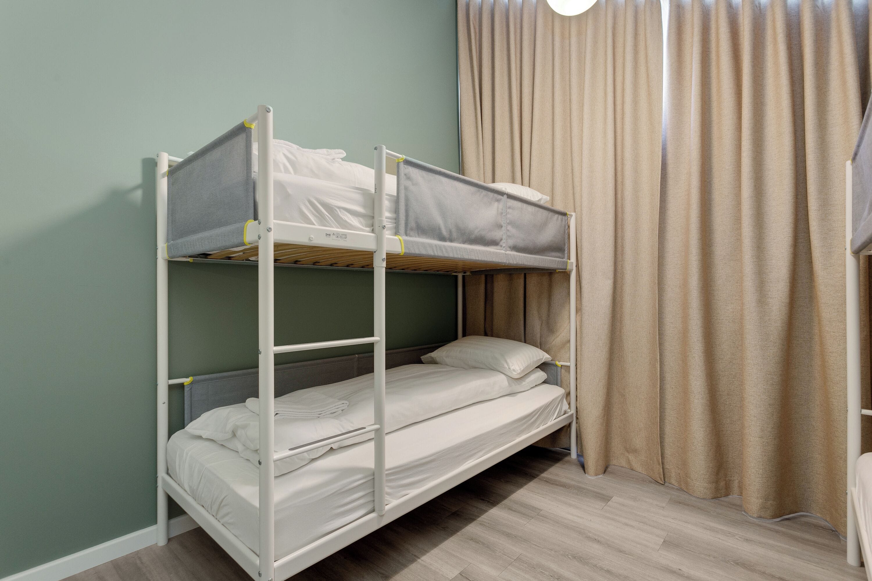 A bunk bed with white bedding in a room with green walls and a curtain.