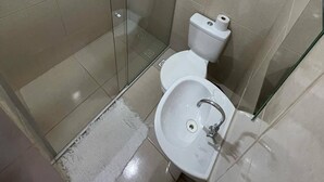 Un baño con cabina de ducha de vidrio, inodoro y lavamanos.
